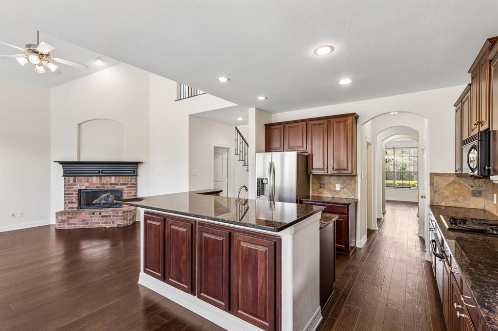960 Remuda Road Frisco, TX 75033 - Photo 28 of 39 Open-concept kitchen and living area featuring wood-finish flooring, a kitchen island with sink and dark wood cabinetry, stainless steel appliances, and a brick fireplace