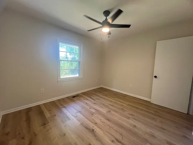 an empty room with wooden floor ceiling fan and windows