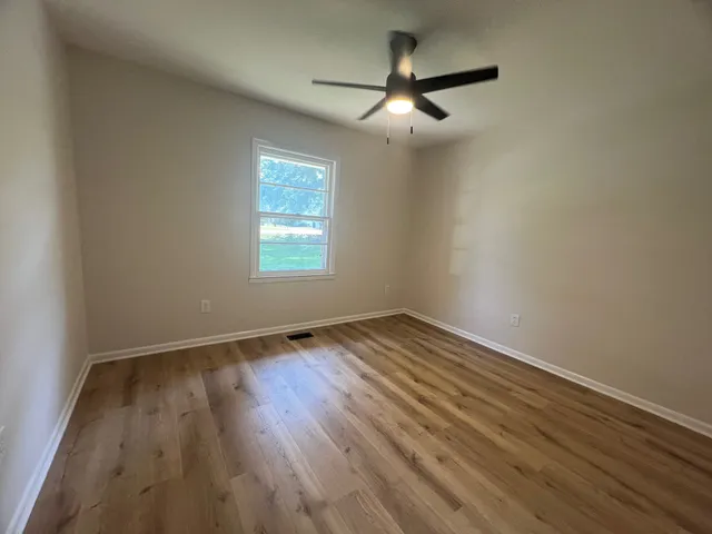 an empty room with wooden floor fan and windows