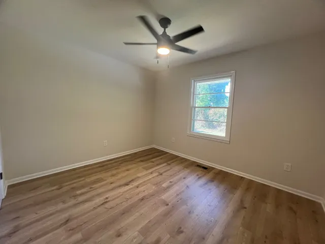 an empty room with wooden floor ceiling fan and windows