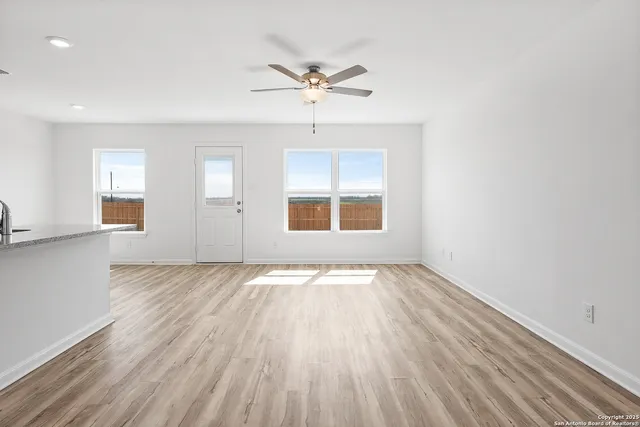 an empty room with wooden floor chandelier fan and windows