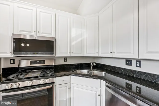 a kitchen with stainless steel appliances granite countertop a stove a sink and white cabinets
