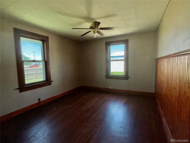 a view of an empty room with wooden floor and a ceiling fan