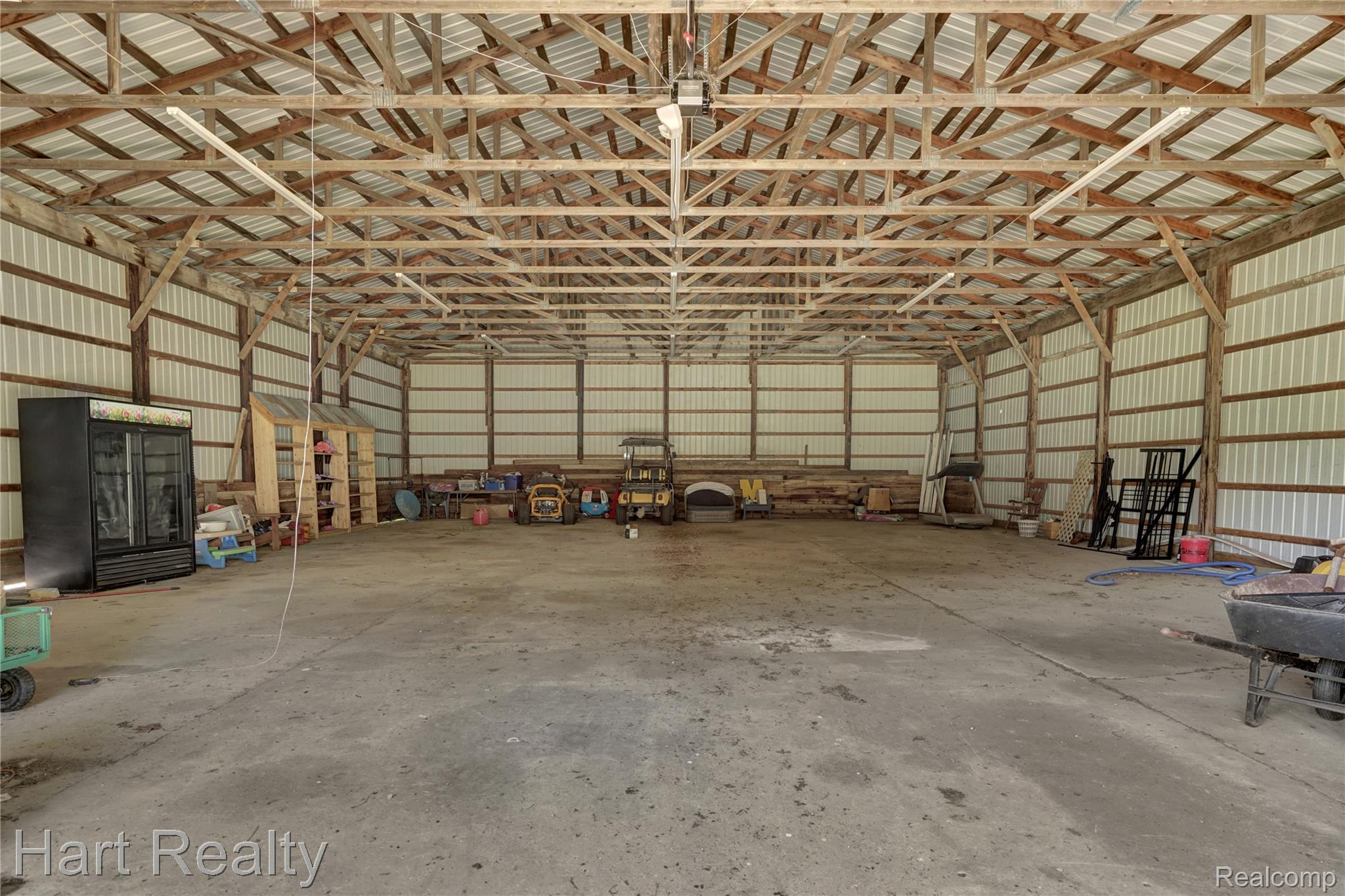 7167 Brown School Road North Branch, MI 48461 - Photo 42 of 51 Expansive open-span structure featuring a wood-beam ceiling, exposed metal roof, corrugated metal wall panels, concrete flooring, and fluorescent strip lighting