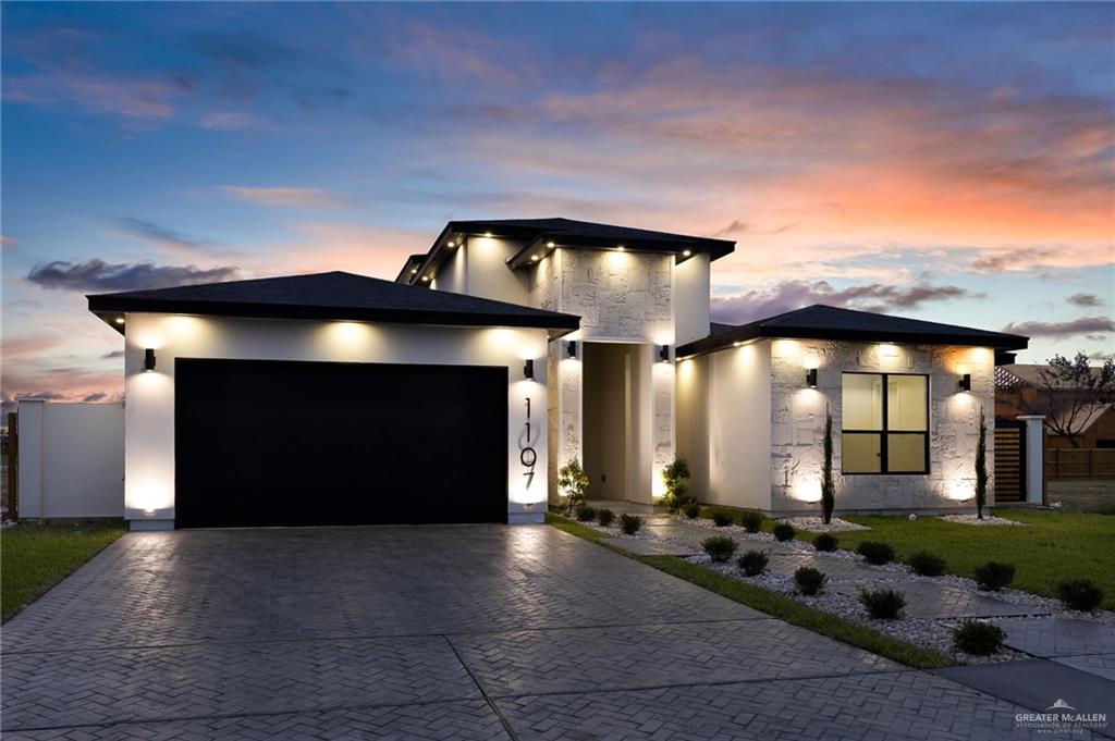 1107 Benjamin Street Mission, TX 78573 - Photo 2 of 19 Contemporary exterior featuring a black garage door, stamped concrete driveway, stone facade accents, recessed lighting, and manicured landscaping