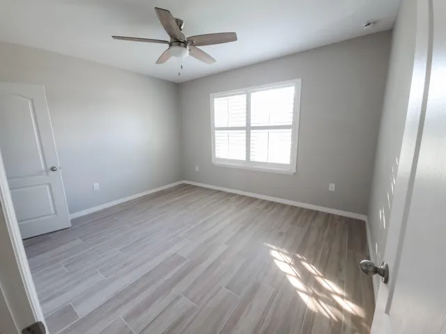 an empty room with wooden floor fan and windows