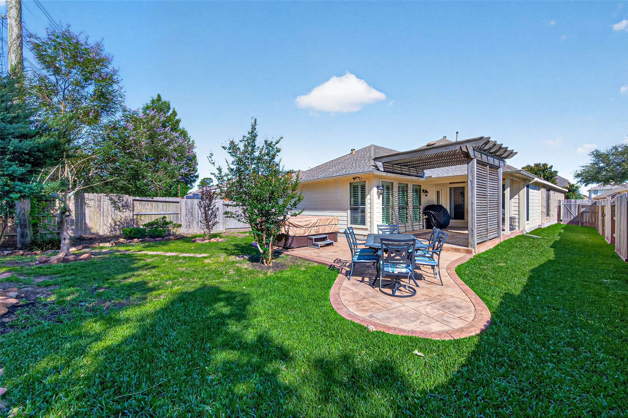 27443 Rebecca Field Lane Spring, TX 77386 - Photo 28 of 31 Charming backyard with a well-maintained lawn, a cozy patio area featuring a dining set, and a wooden pergola for shade, perfect for outdoor gatherings and relaxation.