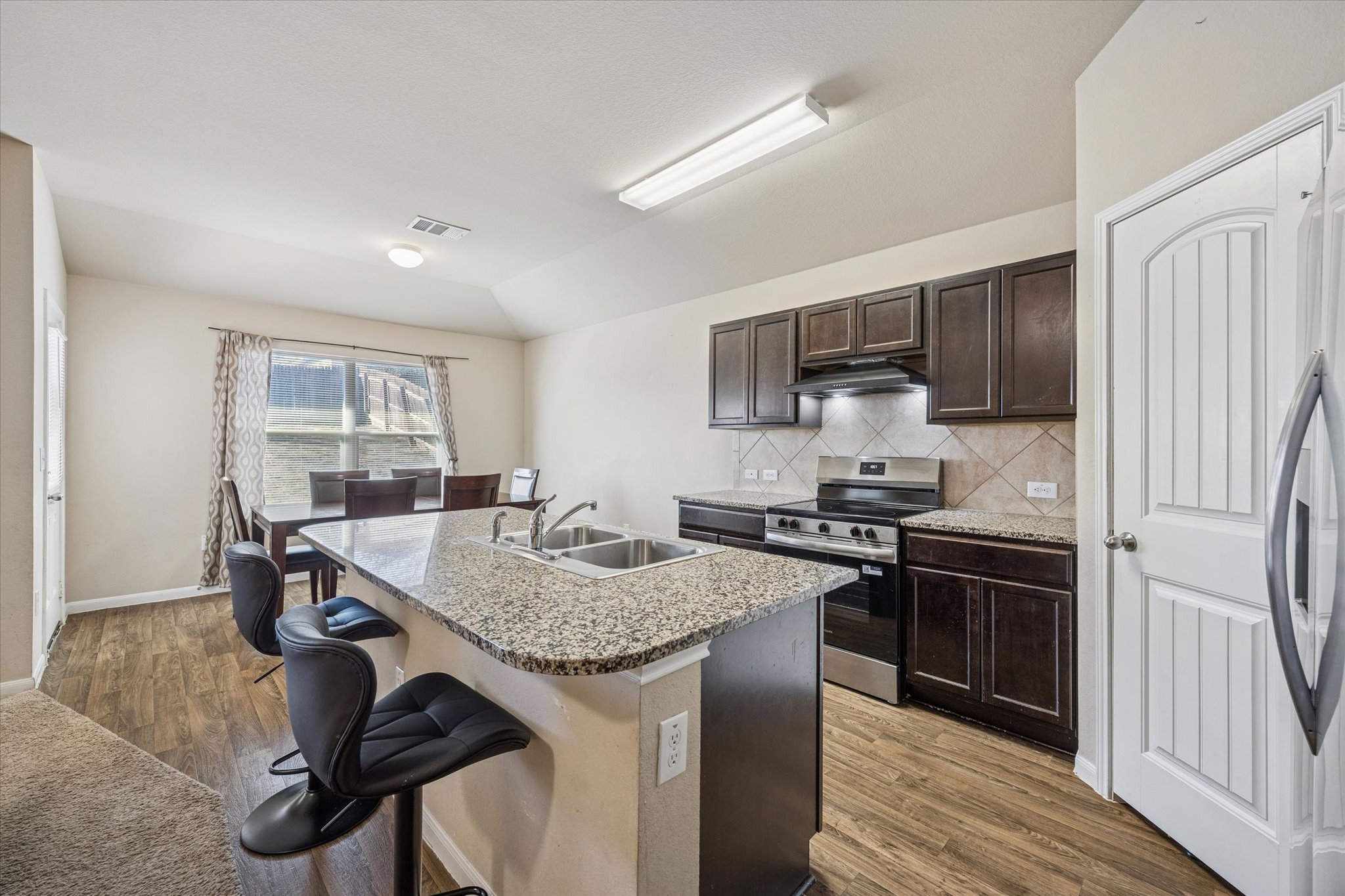 15211 Wideleaf Cove Austin, TX 78724 - Photo 7 of 15 a kitchen with kitchen island granite countertop a stove top oven a sink dishwasher a dining table and chairs with wooden floor