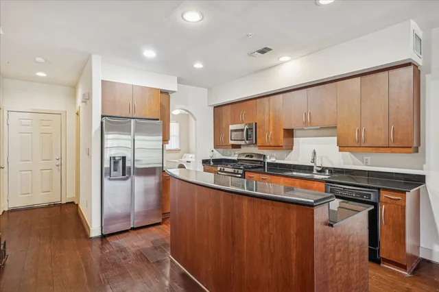 a kitchen with stainless steel appliances granite countertop a refrigerator a sink dishwasher a stove and white countertops with wooden floor