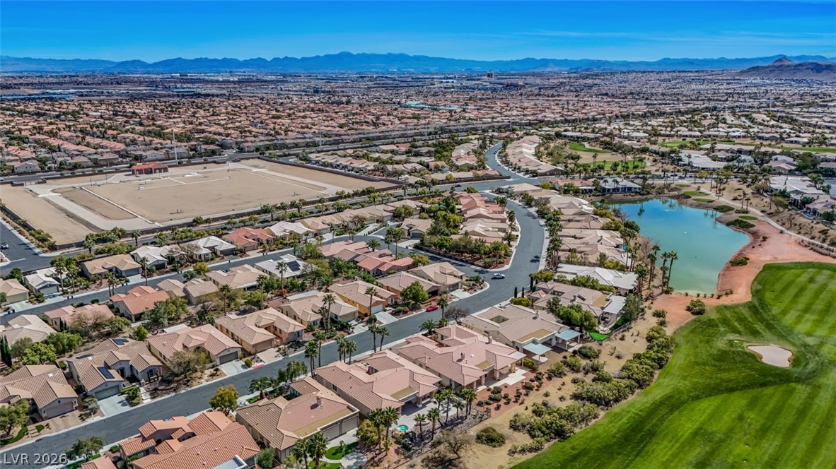 5015 Rivedro Street Las Vegas, NV 89135 - Photo 76 of 91 An aerial perspective reveals a vibrant community with homes, a golf course, and a tranquil lake, all set against a distant mountain range.