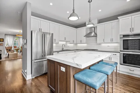 a kitchen with stainless steel appliances granite countertop a refrigerator a sink dishwasher a stove and white countertops with wooden floor