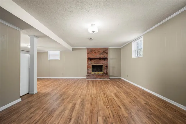 an empty room with wooden floor fireplace and windows
