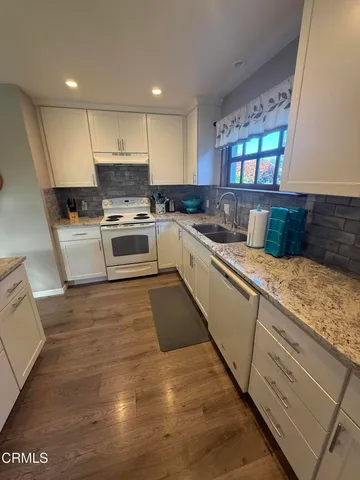 a large white kitchen with stainless steel appliances granite countertop a stove and a sink
