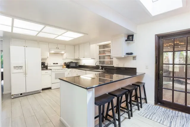 a kitchen with granite countertop white cabinets white appliances a sink and a window