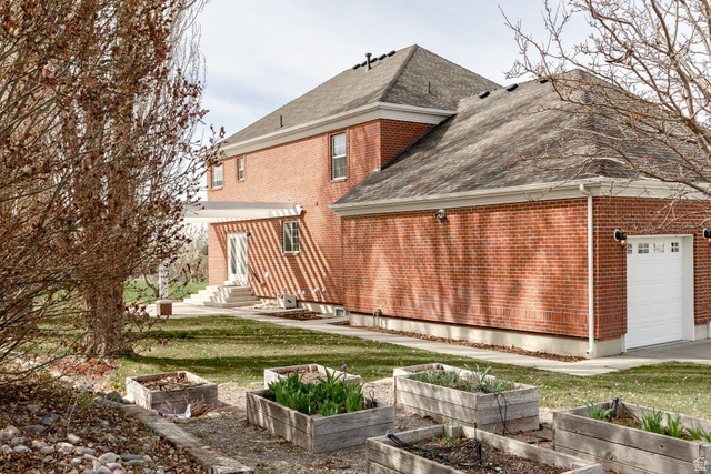 434 Cardon Ridge Drive Smithfield, UT 84335 - Photo 49 of 59 Rear view of house featuring a garden, a shingled roof, brick siding, and a garage