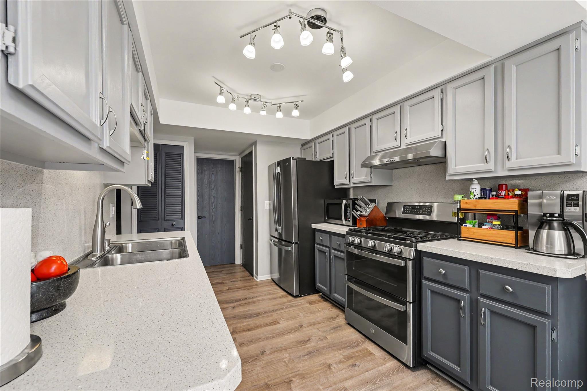 Kitchen featuring light grey upper cabinetry, dark grey lower cabinetry, light-toned countertops, and wood-finish flooring