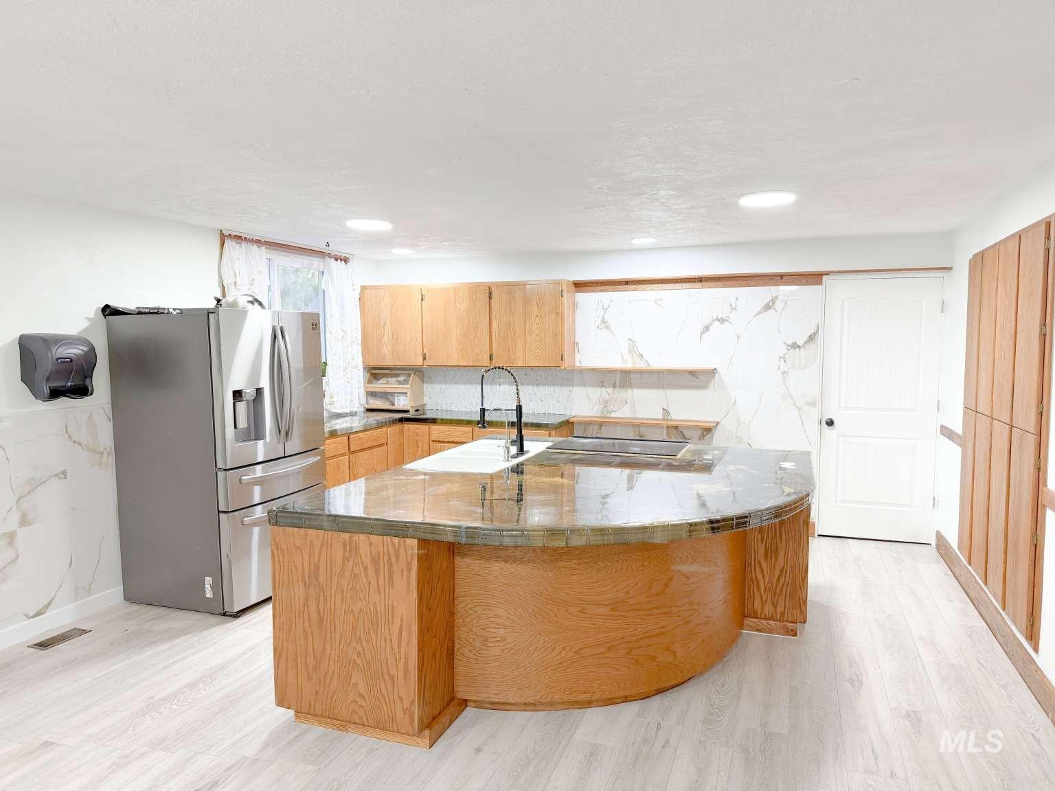 1158 South Powerline Road Nampa, ID 83686 - Photo 14 of 46 Kitchen featuring a curved central island with a polished countertop, light wood-finish cabinetry, and a stainless steel refrigerator