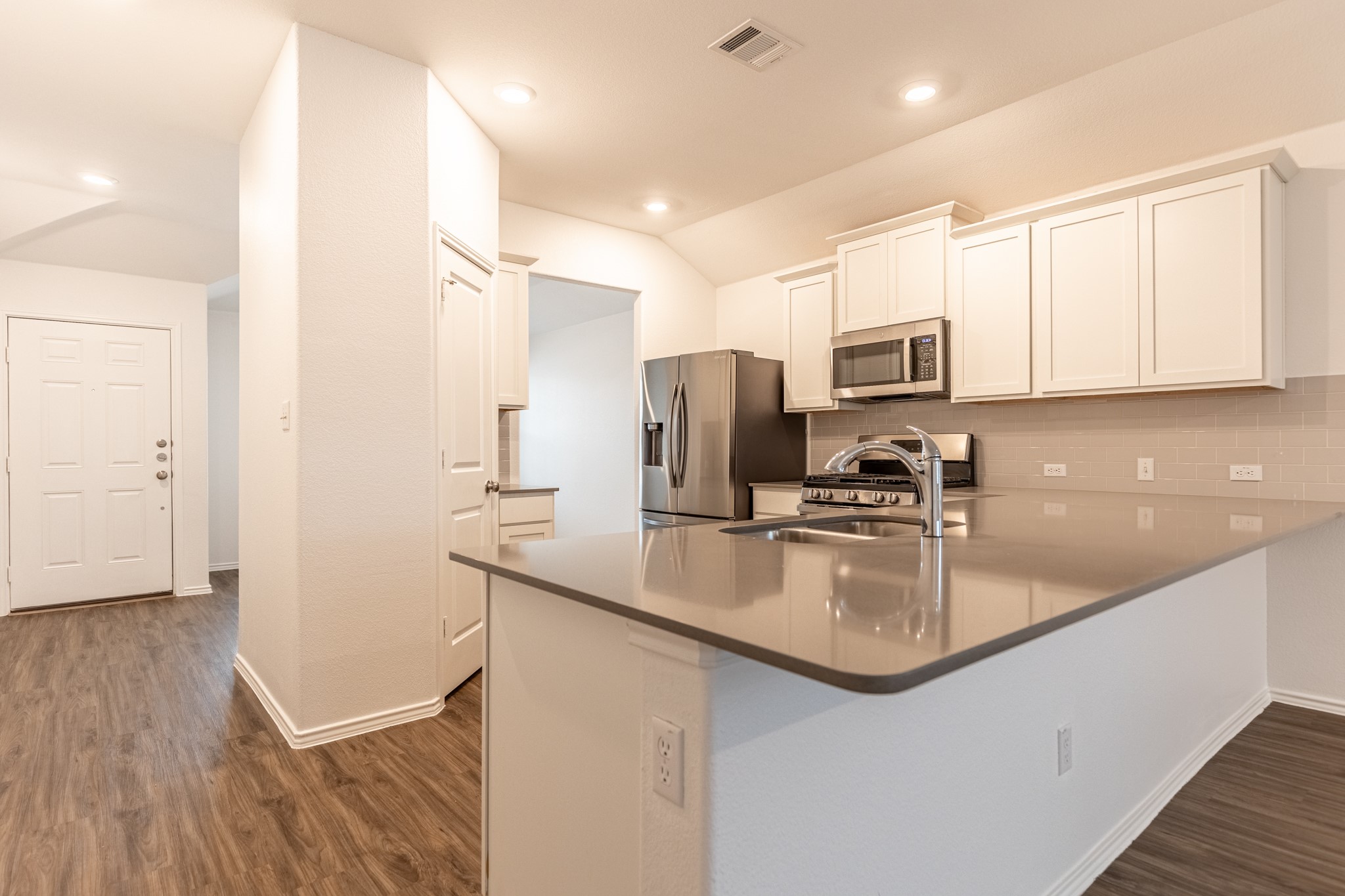 175 Silver Springs Bend Kyle, TX 78640 - Photo 12 of 33 Kitchen with a peninsula, stainless steel appliances, white cabinetry, dark wood-style flooring, and tasteful backsplash