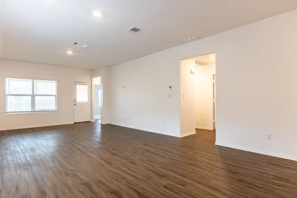 an empty room with wooden floor and windows with curtains