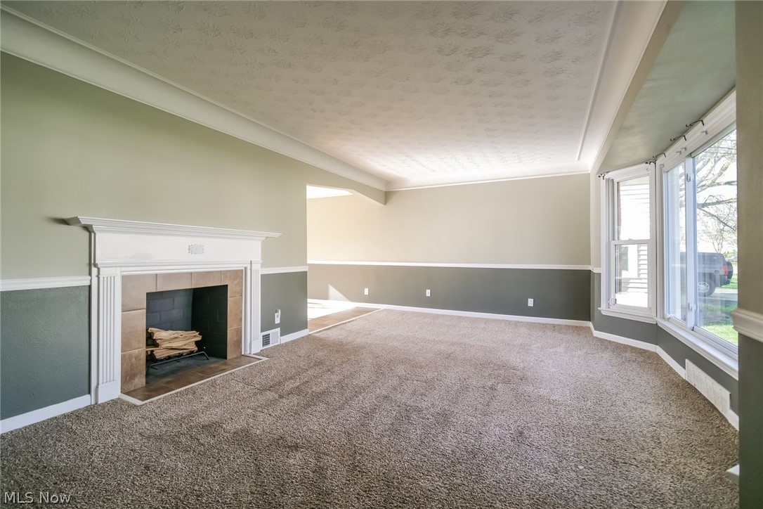 736 Quilliams Road Cleveland Heights, OH 44121 - Photo 3 of 20 Unfurnished living room featuring a textured ceiling, dark carpet, and a tiled fireplace