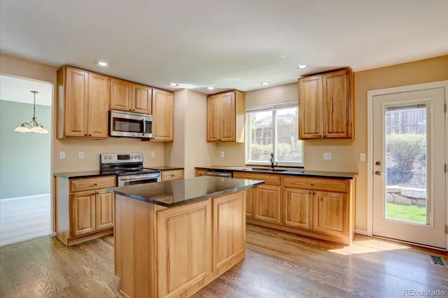 a kitchen with stainless steel appliances granite countertop white cabinets a sink a stove a refrigerator and microwave with wooden floor