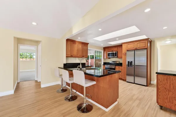 a kitchen with stainless steel appliances granite countertop a refrigerator a stove top oven a sink dishwasher and white cabinets with wooden floor
