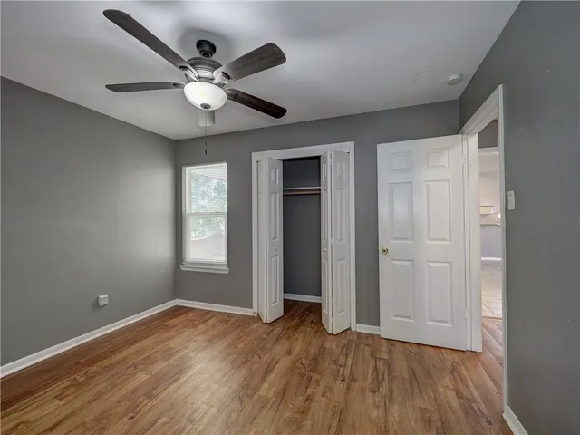 a view of an empty room with wooden floor and a ceiling fan