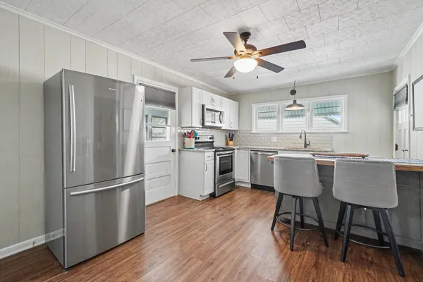 a kitchen with stainless steel appliances granite countertop a refrigerator a sink dishwasher a stove and white countertops with wooden floor