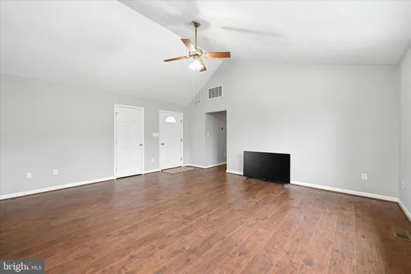 a view of an empty room with wooden floor and a ceiling fan