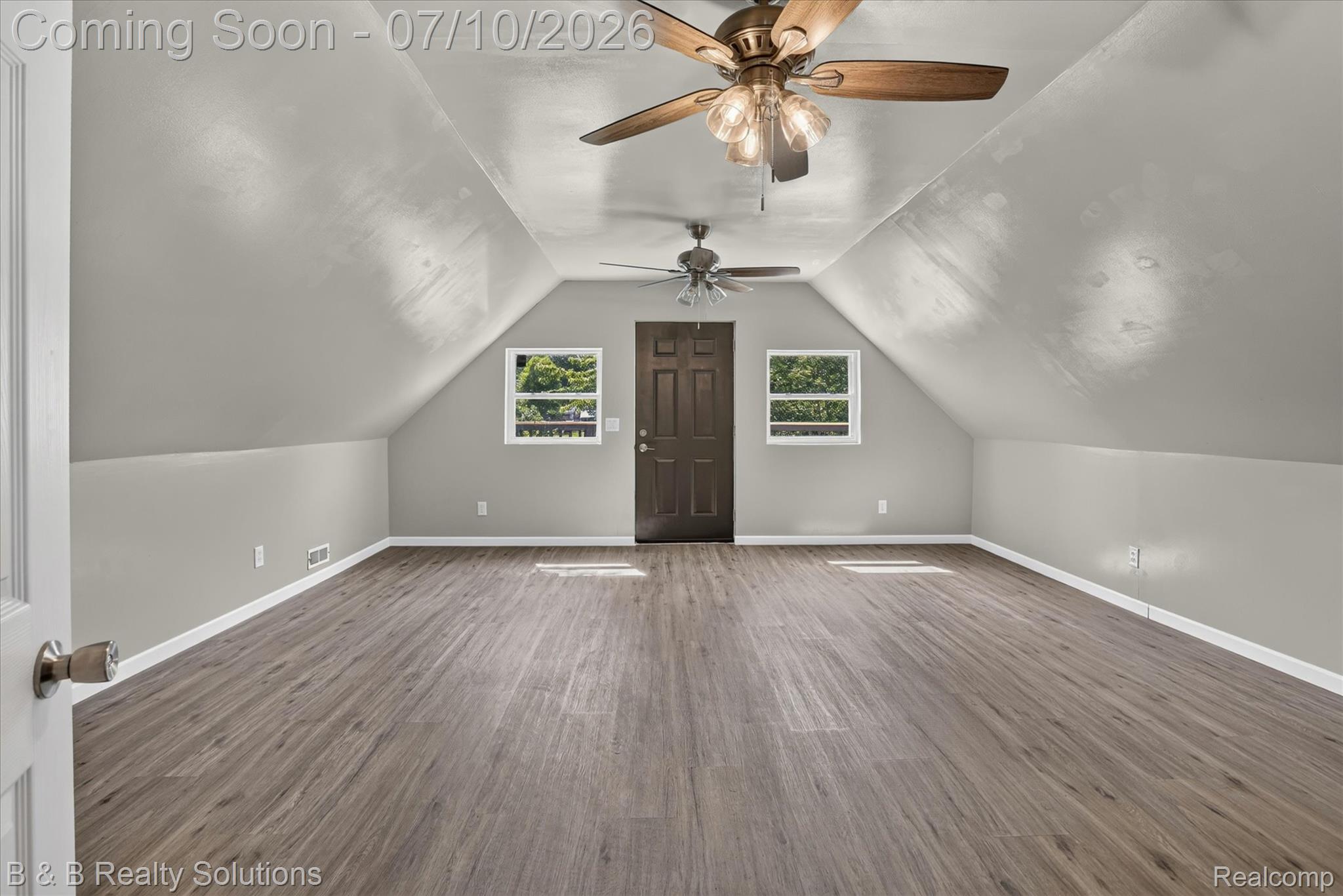 1564 East Burnside Road North Branch, MI 48461 - Photo 5 of 25 Expansive room featuring wood-finish flooring, two ceiling fans, a gabled ceiling, a dark paneled door, and two windows