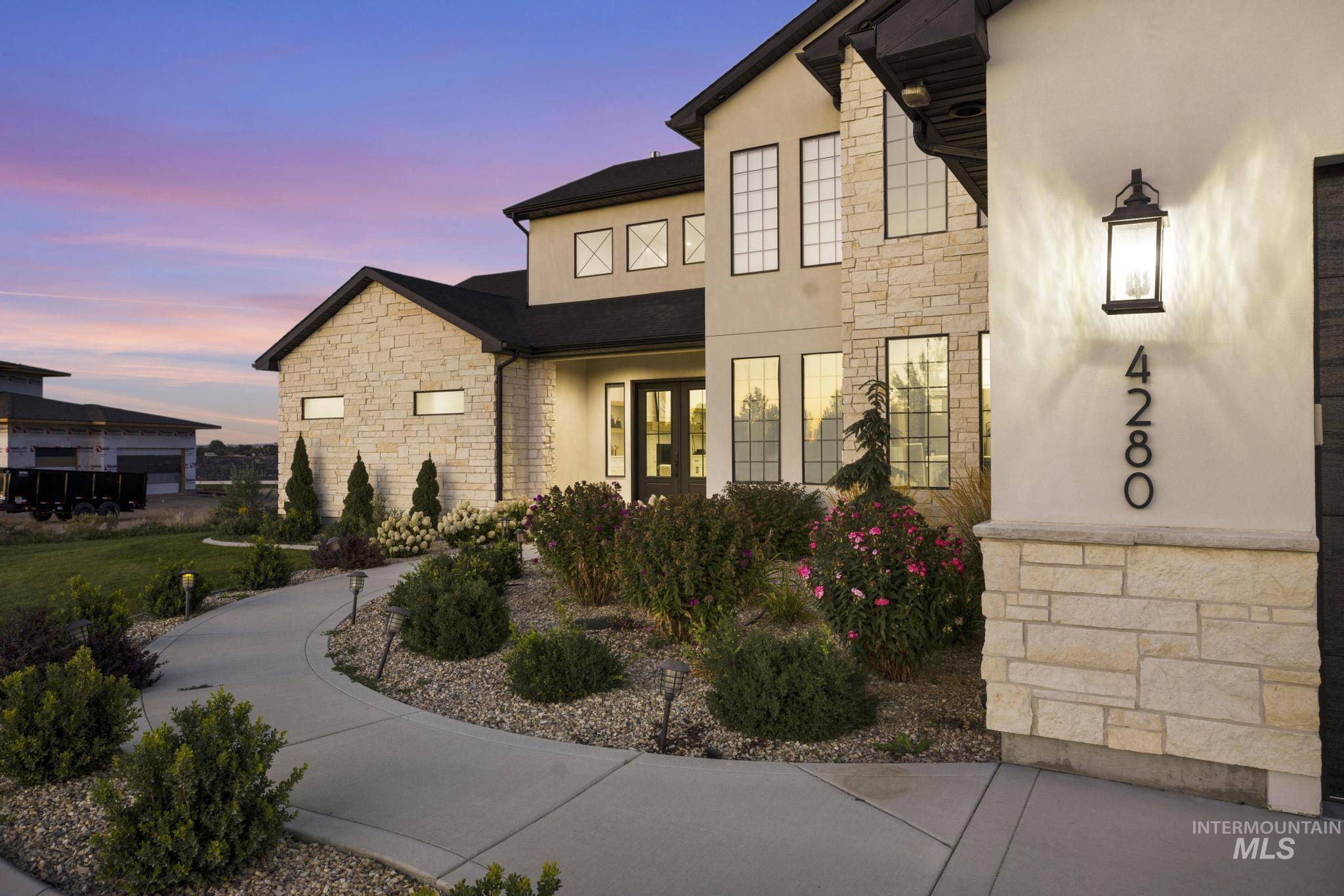 Stucco and stone exterior featuring multiple window styles, established landscaping, a concrete pathway, and an exterior wall lantern