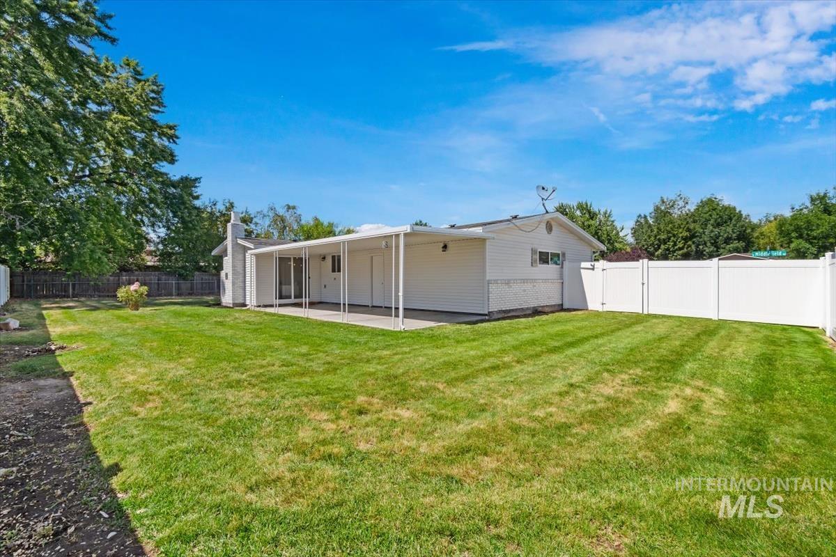 2217 North Middlefield Road Boise, ID 83704 - Photo 33 of 34 Expansive backyard featuring a large green lawn, covered patio, white vinyl fencing, mature trees, and a white siding exterior