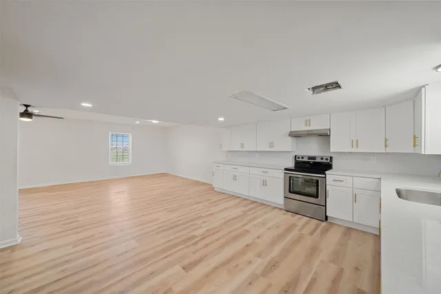 a kitchen with stainless steel appliances granite countertop a stove top oven a sink and white cabinets with wooden floor