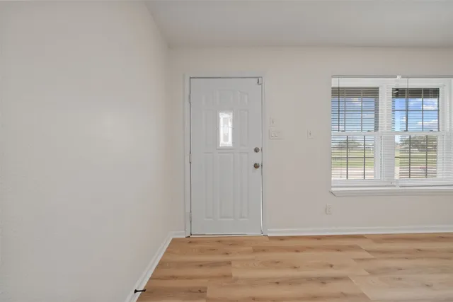 a view of an empty room with wooden floor and a window