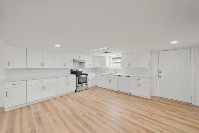 a large white kitchen with granite countertop white cabinets and wooden floor