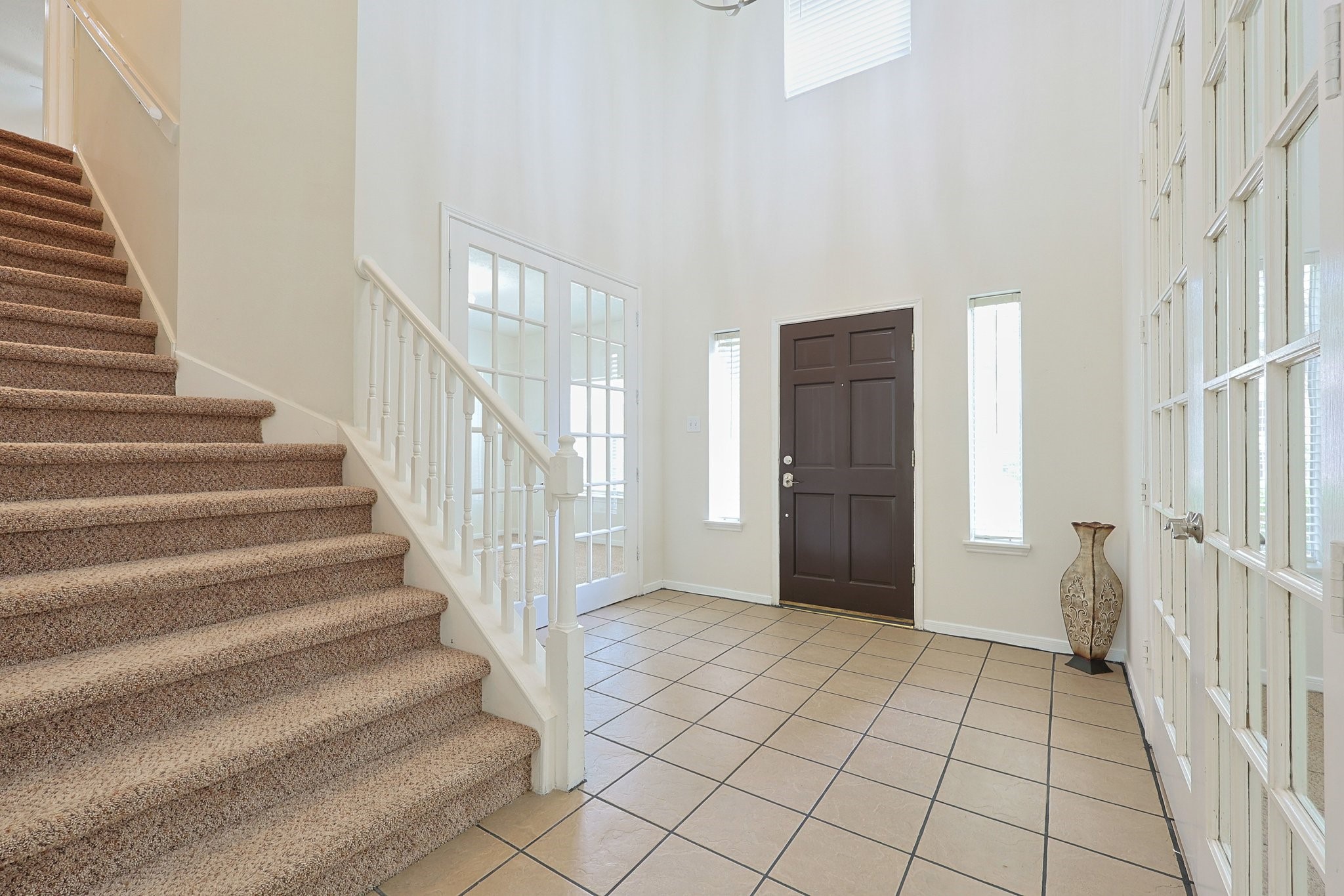 23019 Eastgate Village Drive Spring, TX 77373 - Photo 5 of 46 Entryway features a spacious, tiled foyer with high ceilings, a wooden front door, and two narrow windows. It includes a carpeted staircase with white railings and glass-paneled double doors leading to an adjacent room.