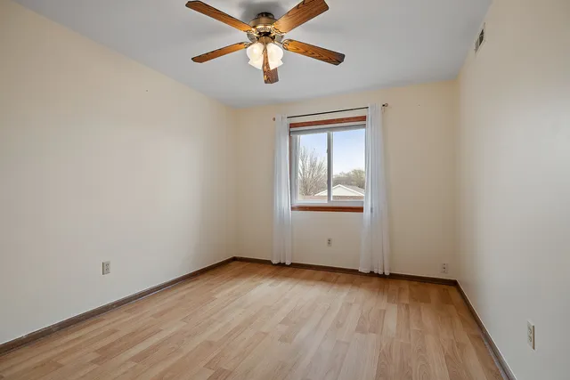 an empty room with wooden floor chandelier fan and windows