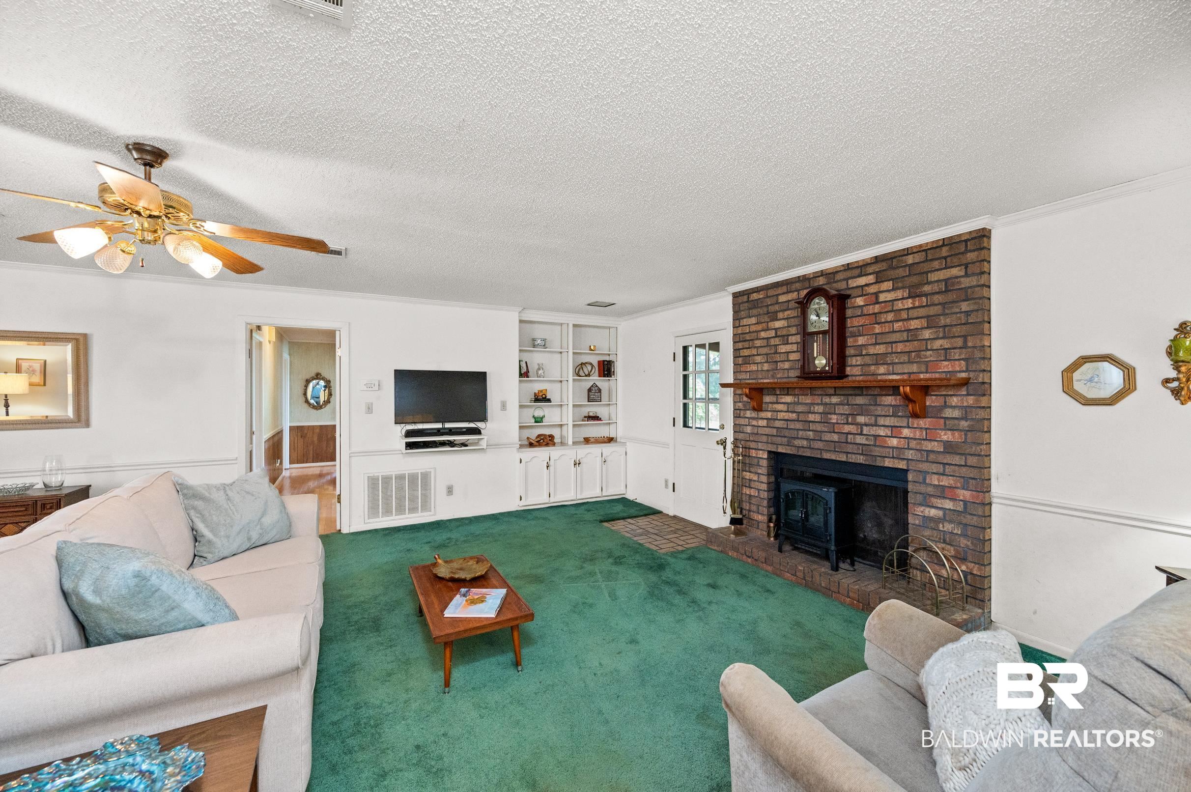 15600 Fackler Road Loxley, AL 36551 - Photo 42 of 51 Carpeted living room with a brick fireplace, built in shelves, a wood stove, a textured ceiling, and ceiling fan