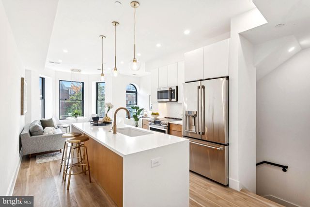 a kitchen with stainless steel appliances granite countertop a refrigerator a sink dishwasher a oven and a dining table with wooden floor