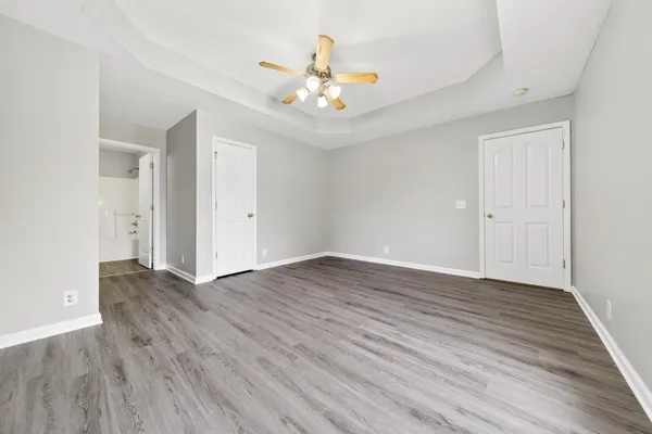 an empty room with wooden floor chandelier fan and windows