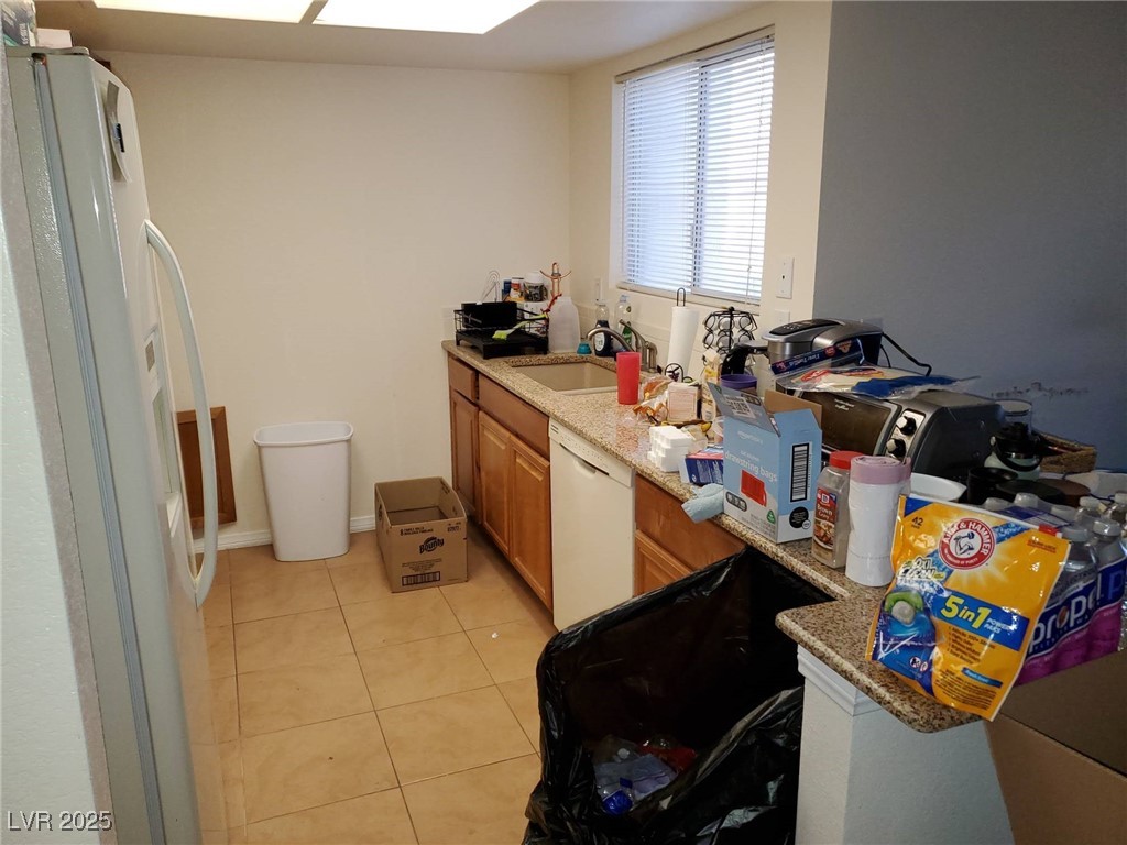 8070 West Russell Road, Unit 1005 Las Vegas, NV 89113 - Photo 11 of 12 Kitchen with white appliances, light tile patterned floors, light stone counters, and brown cabinetry