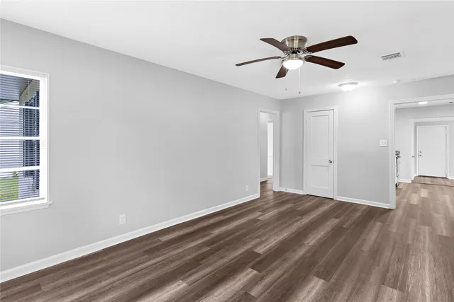 a view of an empty room with wooden floor and a ceiling fan