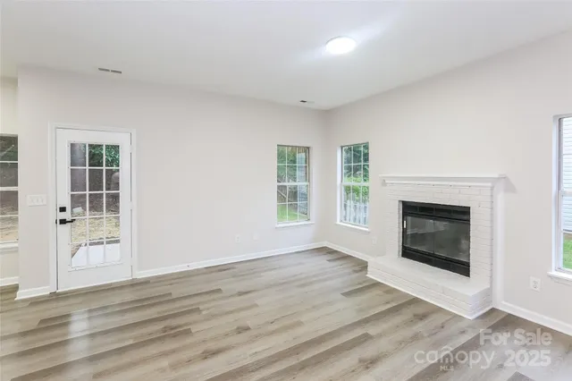 a view of an empty room with wooden floor fireplace and a window