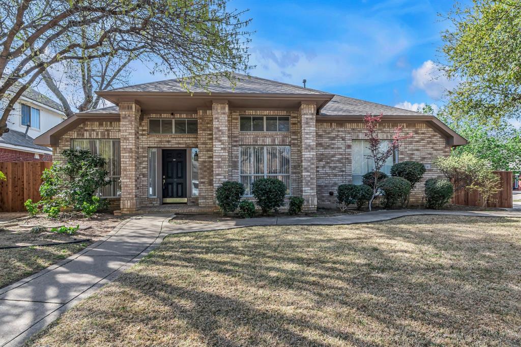 View of front of house featuring roof with shingles, brick siding, a front yard, and fence