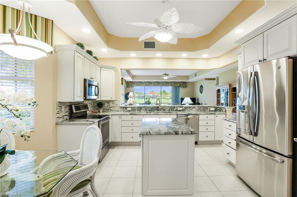 8609 Champions Point, Unit 201 Naples, FL 34113 - Photo 8 of 25 a kitchen with stainless steel appliances kitchen island granite countertop a refrigerator a stove a sink dishwasher and white cabinets with wooden floor