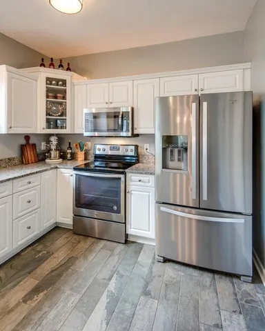 a kitchen with stainless steel appliances granite countertop a refrigerator a stove a sink and white cabinets