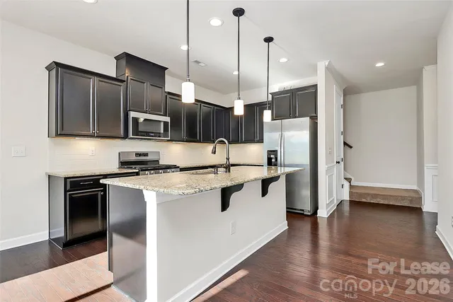 a kitchen with stainless steel appliances granite countertop a sink a stove a refrigerator and island with wooden floor