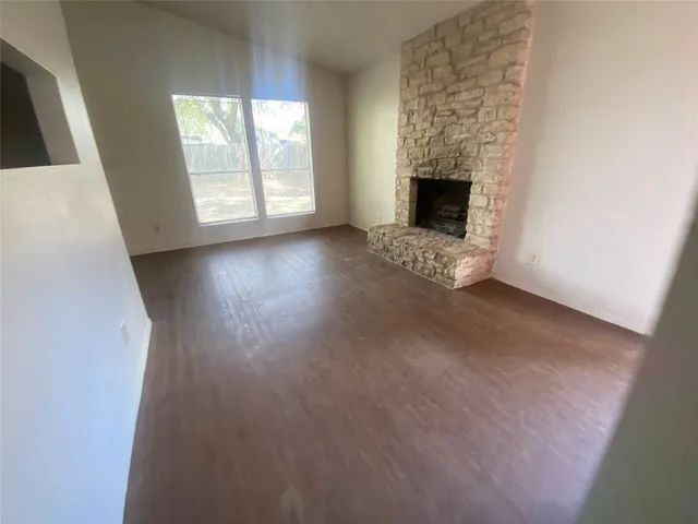an empty room with wooden floor fireplace and windows