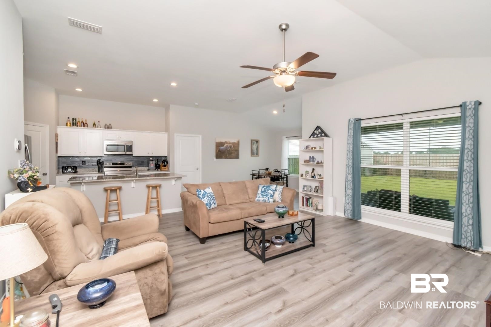 1295 Hayward Loop Foley, AL 36535 - Photo 6 of 29 Open-concept living area featuring wood-finish flooring, vaulted ceilings, and a kitchen with white cabinetry and stainless steel appliances