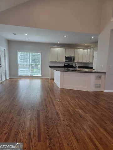 a kitchen with stainless steel appliances granite countertop a stove top oven a sink and a microwave oven on the wooden floor